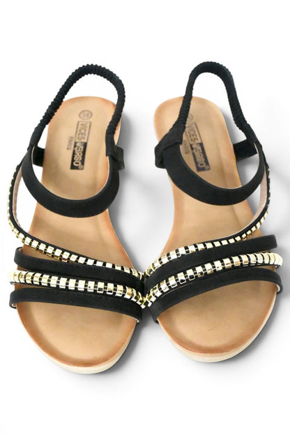 sandalia de talla grande para mujer de color negro y diseño de tiras en el empeine decoradas con tachuelas doradas y el agarre al tobillo elástico, cuña y suela acolchada