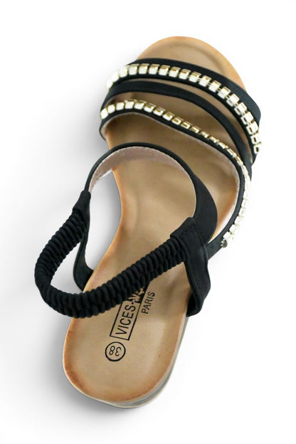 sandalia de mujer en color negro con diseño de tiras en el empeine decoradas con tachuelas doradas y elástico en el tobillo suela acolchada perfecta para eventos, disponible desde la talla 38 a la 43